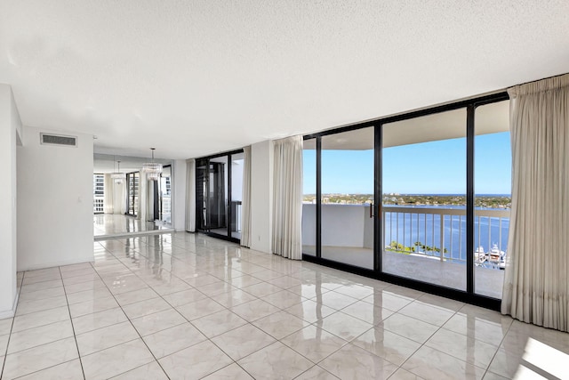 spare room featuring a water view, a wall of windows, a textured ceiling, and light tile patterned floors