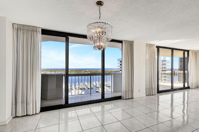 tiled empty room featuring a textured ceiling, a water view, an inviting chandelier, and expansive windows