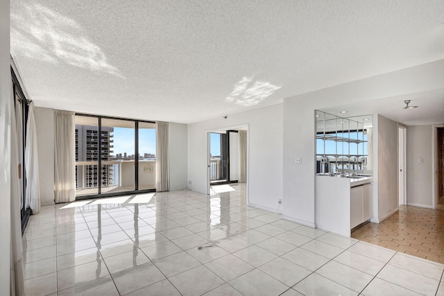 unfurnished room with a textured ceiling, light tile patterned flooring, floor to ceiling windows, and a wealth of natural light