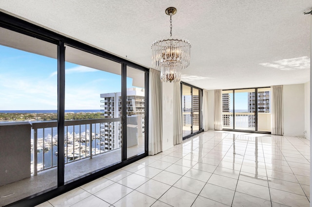 tiled spare room with expansive windows, a textured ceiling, a healthy amount of sunlight, a water view, and an inviting chandelier