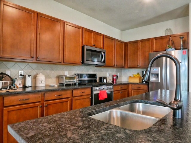 kitchen featuring appliances with stainless steel finishes, backsplash, dark stone counters, and sink