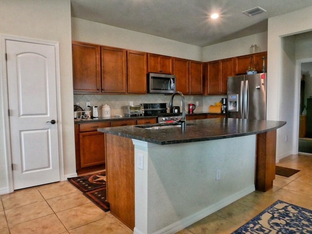 kitchen with light tile patterned flooring, sink, stainless steel appliances, and an island with sink