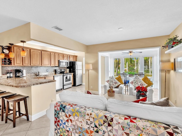 kitchen featuring light tile patterned floors, a breakfast bar area, appliances with stainless steel finishes, ceiling fan, and backsplash