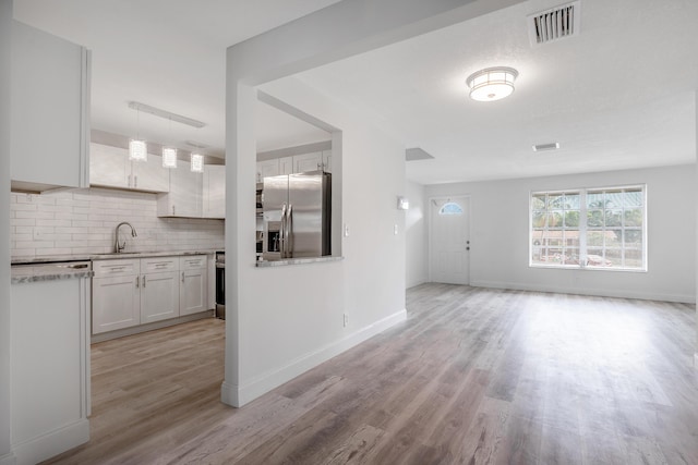 interior space with stainless steel fridge, light wood-type flooring, backsplash, sink, and white cabinetry