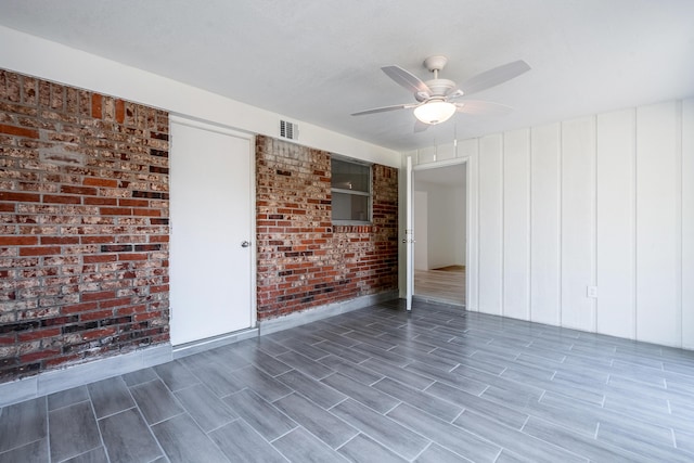 empty room featuring ceiling fan and brick wall