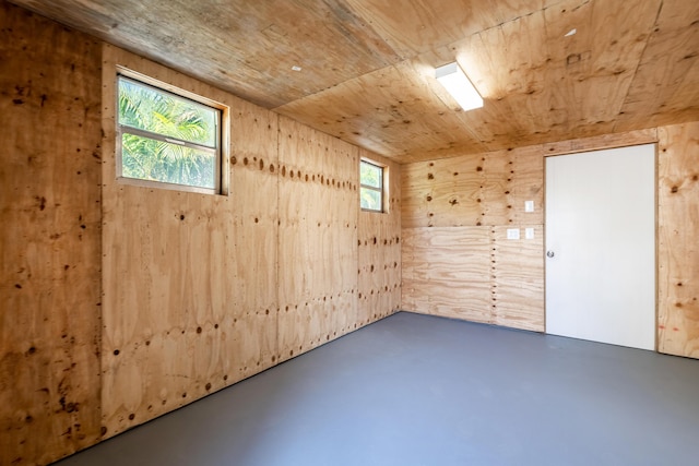 unfurnished room featuring concrete flooring, wooden walls, and wood ceiling