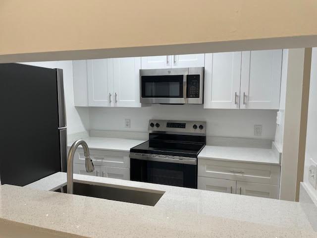 kitchen featuring light stone counters, sink, white cabinetry, and stainless steel appliances