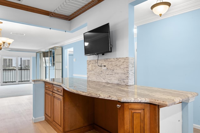 kitchen featuring kitchen peninsula, light stone countertops, ornamental molding, and a notable chandelier