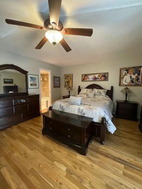 bedroom with ceiling fan, light hardwood / wood-style flooring, ensuite bathroom, and a textured ceiling