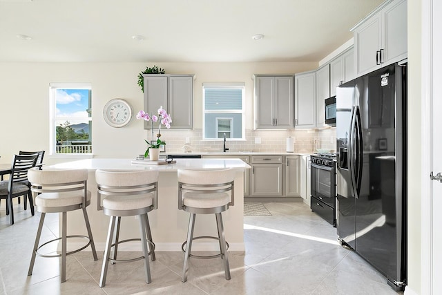 kitchen with gray cabinetry, sink, tasteful backsplash, a kitchen bar, and black appliances