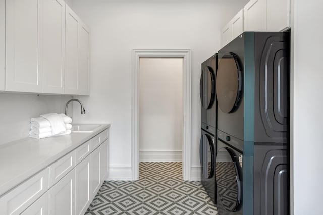 clothes washing area featuring baseboards, a sink, cabinet space, and stacked washer / drying machine