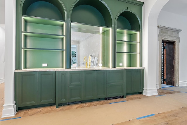 bar with light hardwood / wood-style floors, ornate columns, green cabinets, and sink