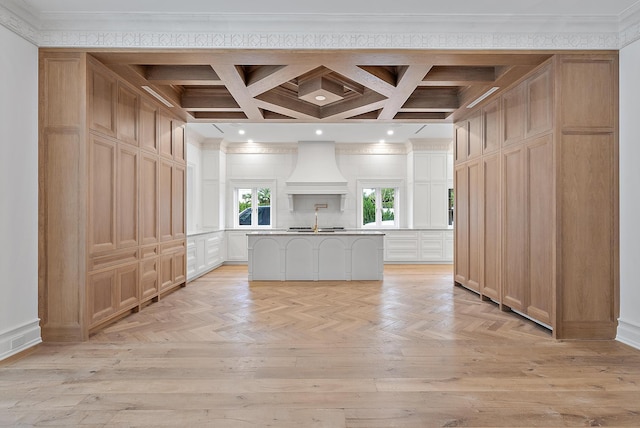 kitchen with a kitchen bar, coffered ceiling, ornamental molding, custom exhaust hood, and a kitchen island with sink