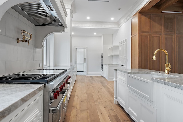 kitchen with white cabinetry, sink, stainless steel stove, and light hardwood / wood-style floors