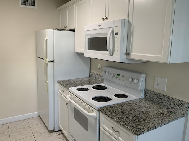 kitchen with white cabinets, light tile patterned floors, white appliances, and dark stone counters