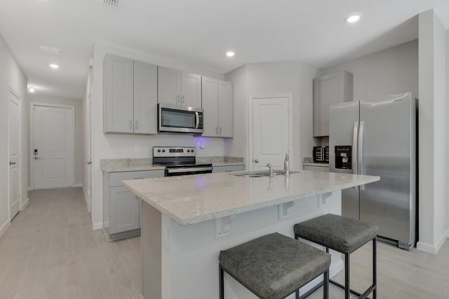 kitchen featuring light stone countertops, sink, stainless steel appliances, and a center island with sink