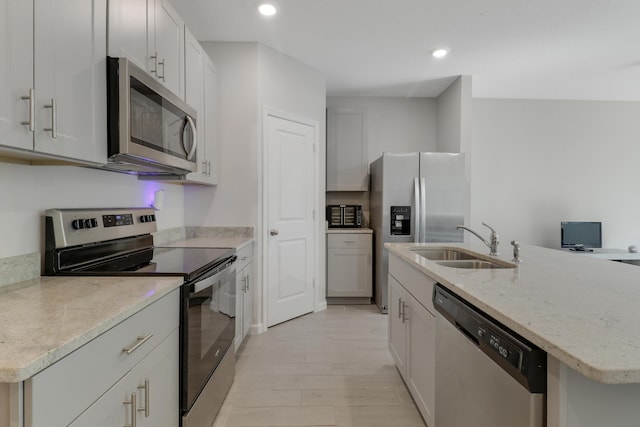 kitchen with a kitchen island with sink, white cabinets, sink, light wood-type flooring, and stainless steel appliances