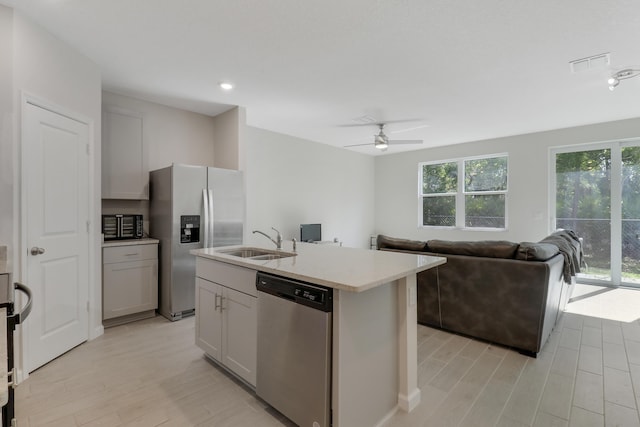 kitchen featuring ceiling fan, sink, stainless steel appliances, light hardwood / wood-style flooring, and an island with sink