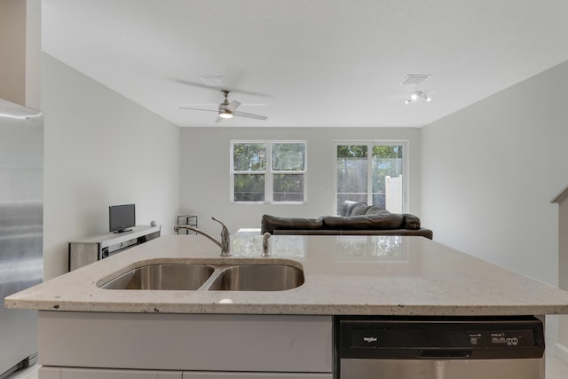 kitchen featuring ceiling fan, sink, stainless steel appliances, light stone counters, and a center island with sink