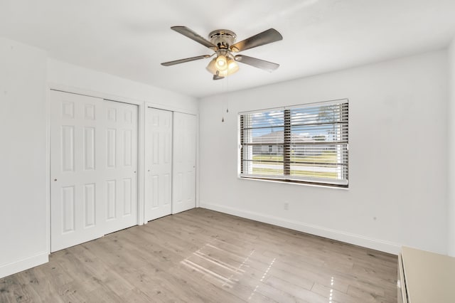 unfurnished bedroom with ceiling fan, light wood-type flooring, and multiple closets