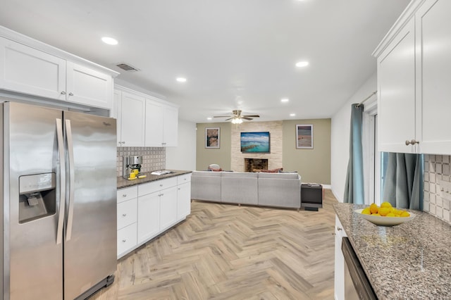 kitchen with decorative backsplash, dark stone counters, stainless steel appliances, ceiling fan, and white cabinetry