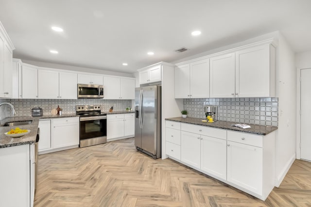 kitchen featuring white cabinets, stainless steel appliances, dark stone countertops, and sink