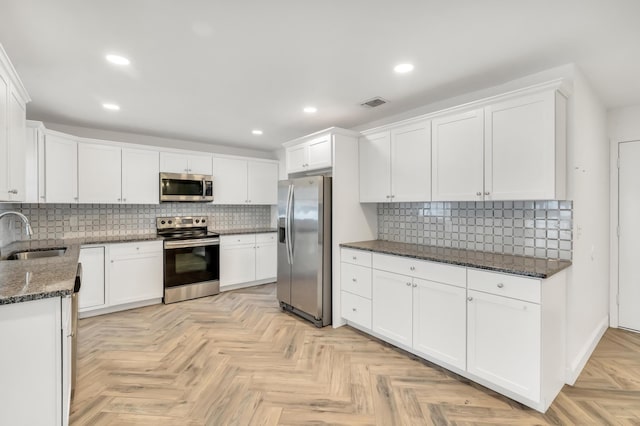 kitchen with decorative backsplash, appliances with stainless steel finishes, sink, dark stone countertops, and white cabinets