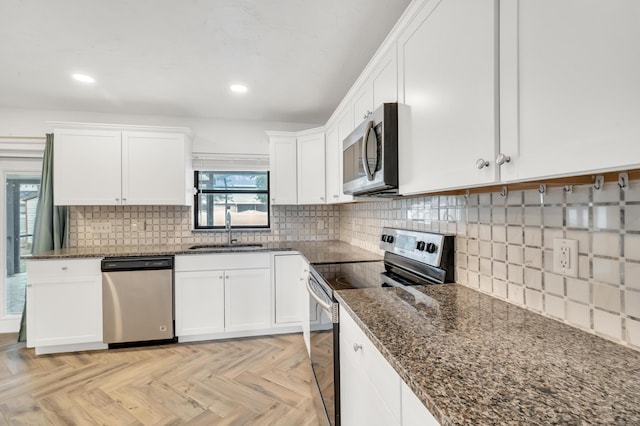 kitchen with light parquet floors, white cabinets, sink, dark stone countertops, and stainless steel appliances