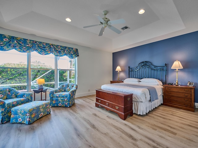 bedroom featuring light hardwood / wood-style flooring, a raised ceiling, and ceiling fan