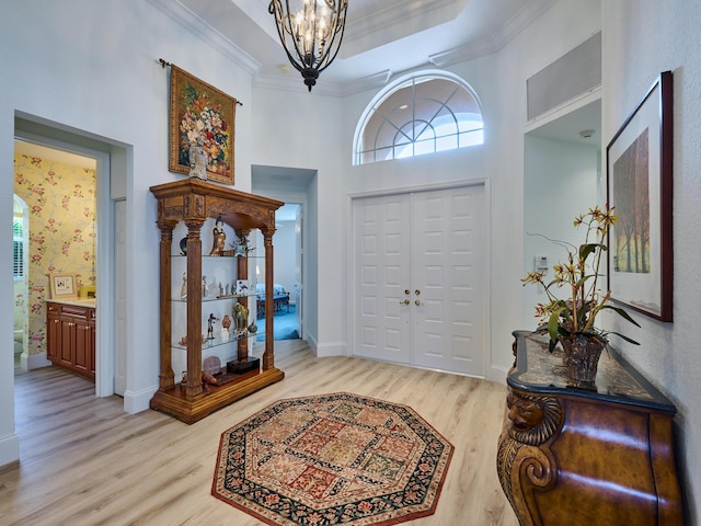 foyer with a chandelier, a high ceiling, light hardwood / wood-style flooring, and ornamental molding