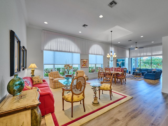 living room with ceiling fan with notable chandelier, light wood-type flooring, and crown molding