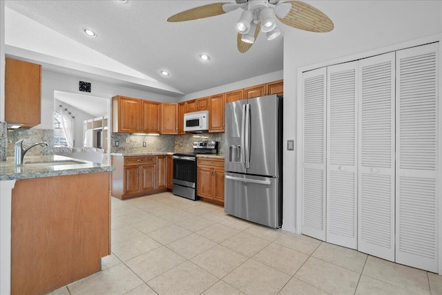 kitchen featuring light stone counters, stainless steel appliances, vaulted ceiling, sink, and light tile patterned floors