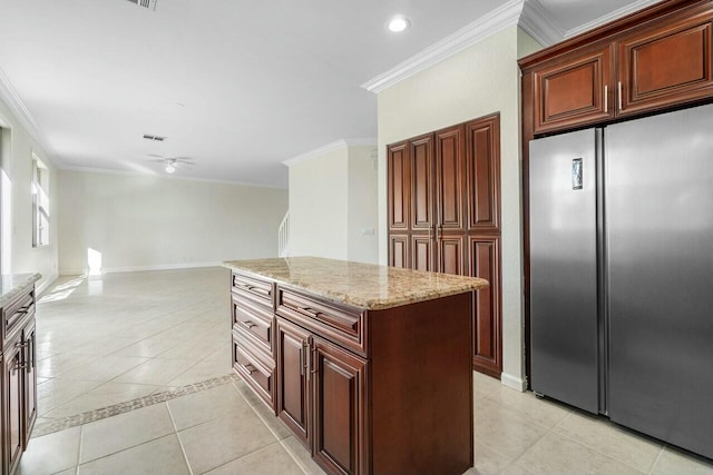 kitchen featuring light stone countertops, stainless steel fridge, ornamental molding, light tile patterned floors, and a kitchen island