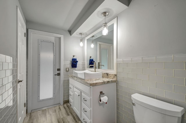 bathroom with wood-type flooring, vanity, toilet, and tile walls