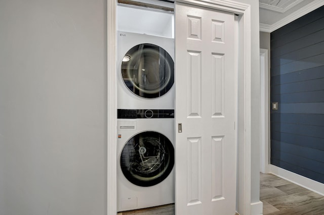 clothes washing area with wooden walls, light hardwood / wood-style flooring, stacked washer / dryer, and ornamental molding