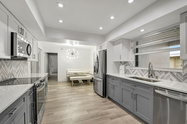 kitchen featuring gray cabinetry, sink, light hardwood / wood-style flooring, decorative backsplash, and appliances with stainless steel finishes