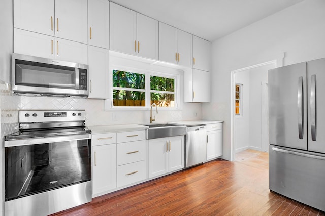 kitchen with appliances with stainless steel finishes, backsplash, sink, white cabinets, and dark hardwood / wood-style floors