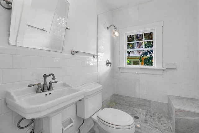 bathroom featuring a tile shower, toilet, tile walls, and sink