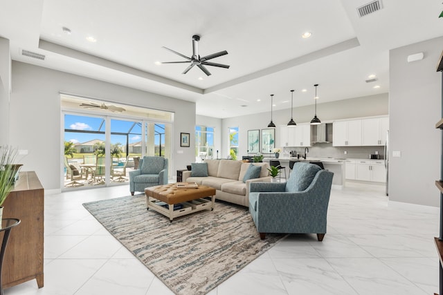 living room with a tray ceiling, ceiling fan, and sink