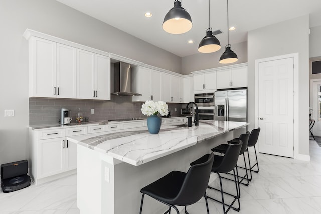 kitchen with white cabinets, appliances with stainless steel finishes, a center island with sink, and wall chimney range hood