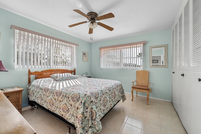 bedroom with ceiling fan, light tile patterned flooring, a textured ceiling, and a closet