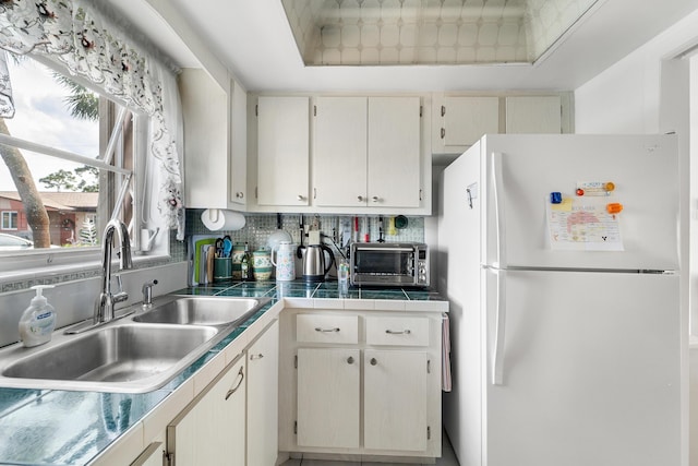 kitchen featuring a raised ceiling, decorative backsplash, sink, and white fridge