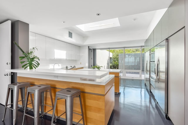 kitchen with white cabinets, sink, appliances with stainless steel finishes, kitchen peninsula, and a breakfast bar area