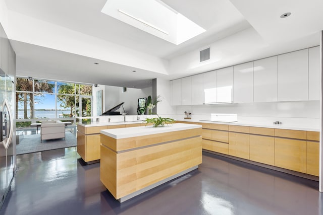 kitchen with a tray ceiling, a skylight, white cabinetry, and a center island