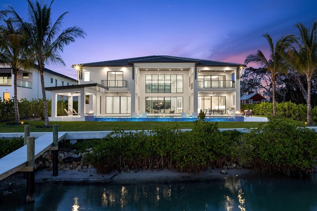 back house at dusk with a balcony, ceiling fan, and a patio area