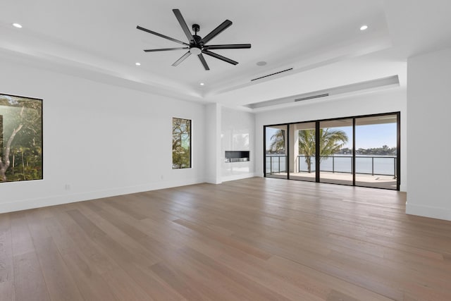 unfurnished living room with a raised ceiling, ceiling fan, and light wood-type flooring