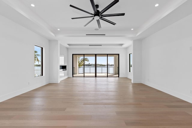 unfurnished living room featuring a raised ceiling, ceiling fan, and light hardwood / wood-style floors