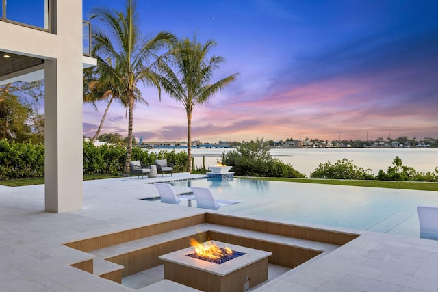 pool at dusk featuring a fire pit, a patio area, and a water view