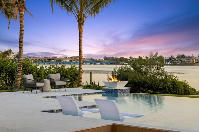 pool at dusk featuring a water view and a patio