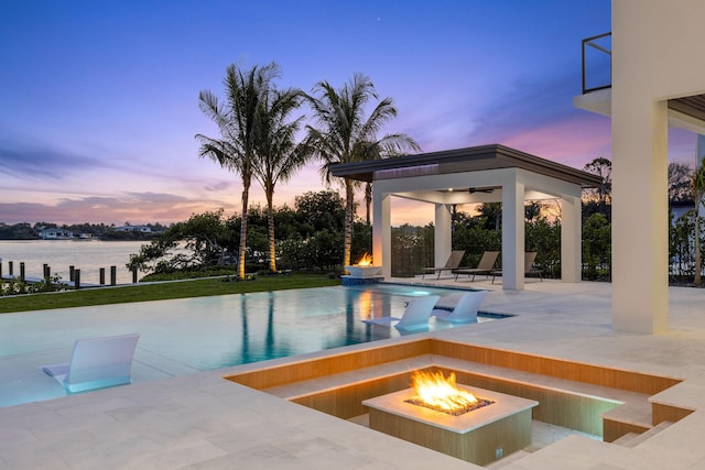 pool at dusk featuring a fire pit, a patio area, a gazebo, and a water view